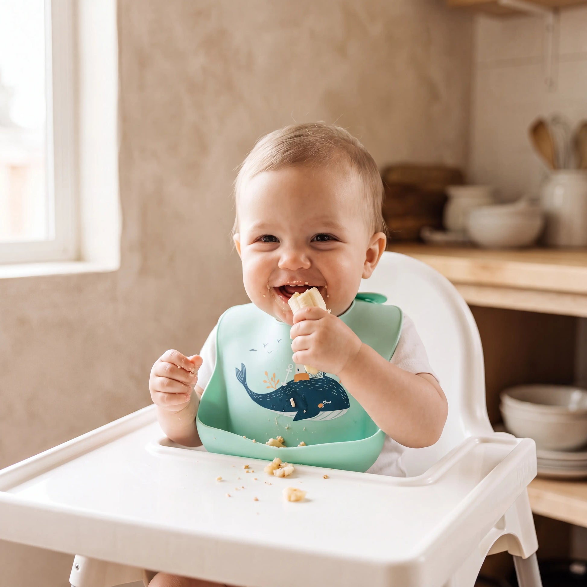 Baby wearing Rahaya whale bib eating in high chair